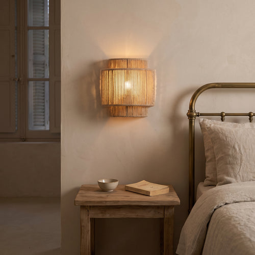 Applique murale en corde de chanvre à étages allumée le soir dans une chambre japandi, de chaque côté du lit